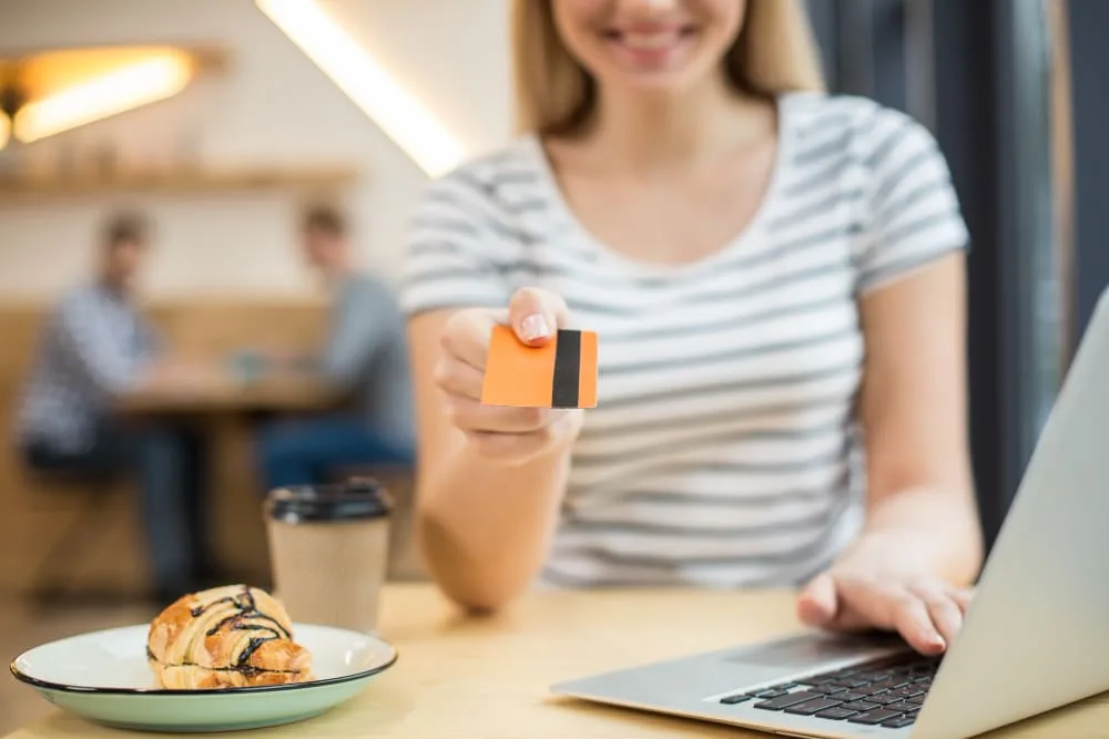 karta kredytowa online kobieta trzyma w prawej ręce pomarańczową kartę